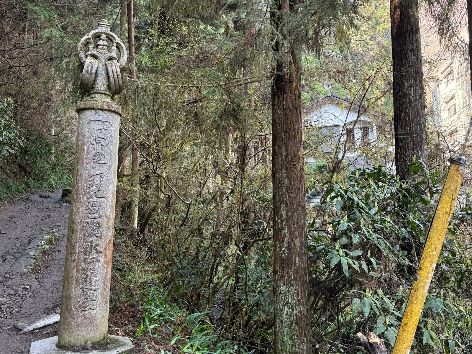 A stone pillar topped with a small carved figure beside Trail 6, in cedar forest