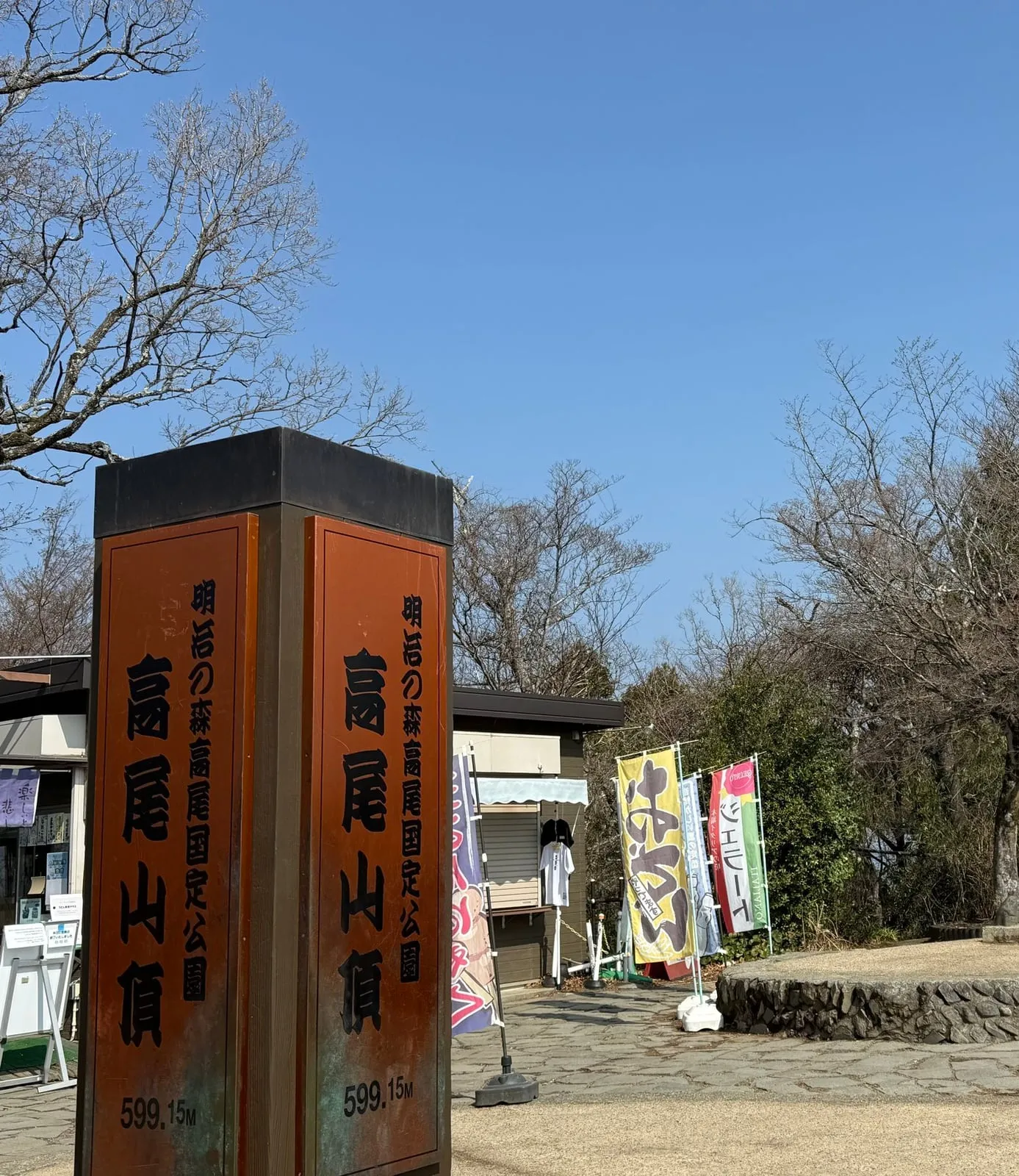 The tall wooden summit post of Mt. Takao, marked 599.15 m, with bare trees behind
