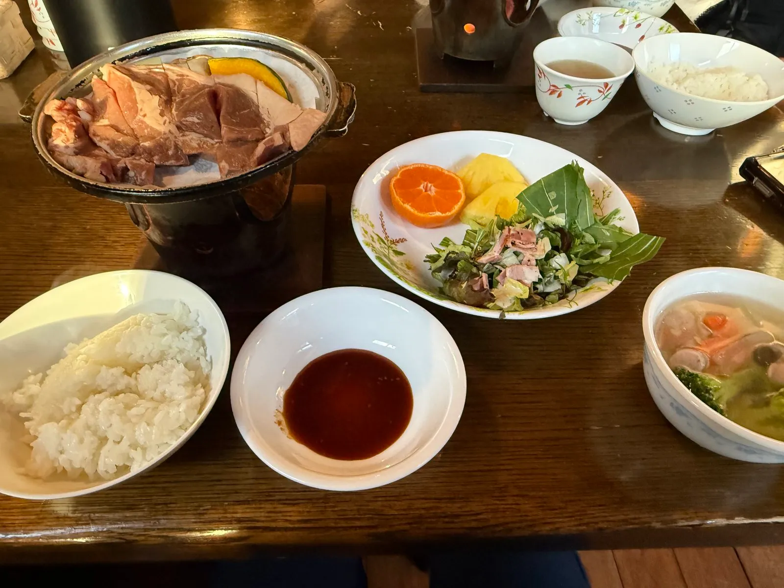 Dinner at Akadake Kosen in March 2026: raw steak and vegetables on an iron plate over a burner, with rice, salad, fruit, soup and dipping sauce