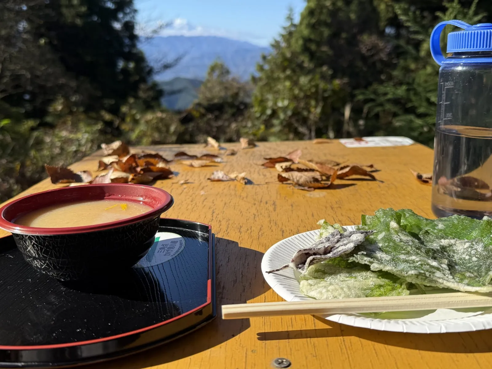 Tempura on a leaf-lined plate and a bowl of nameko soup on a teahouse table, with Mt. Fuji in the distance