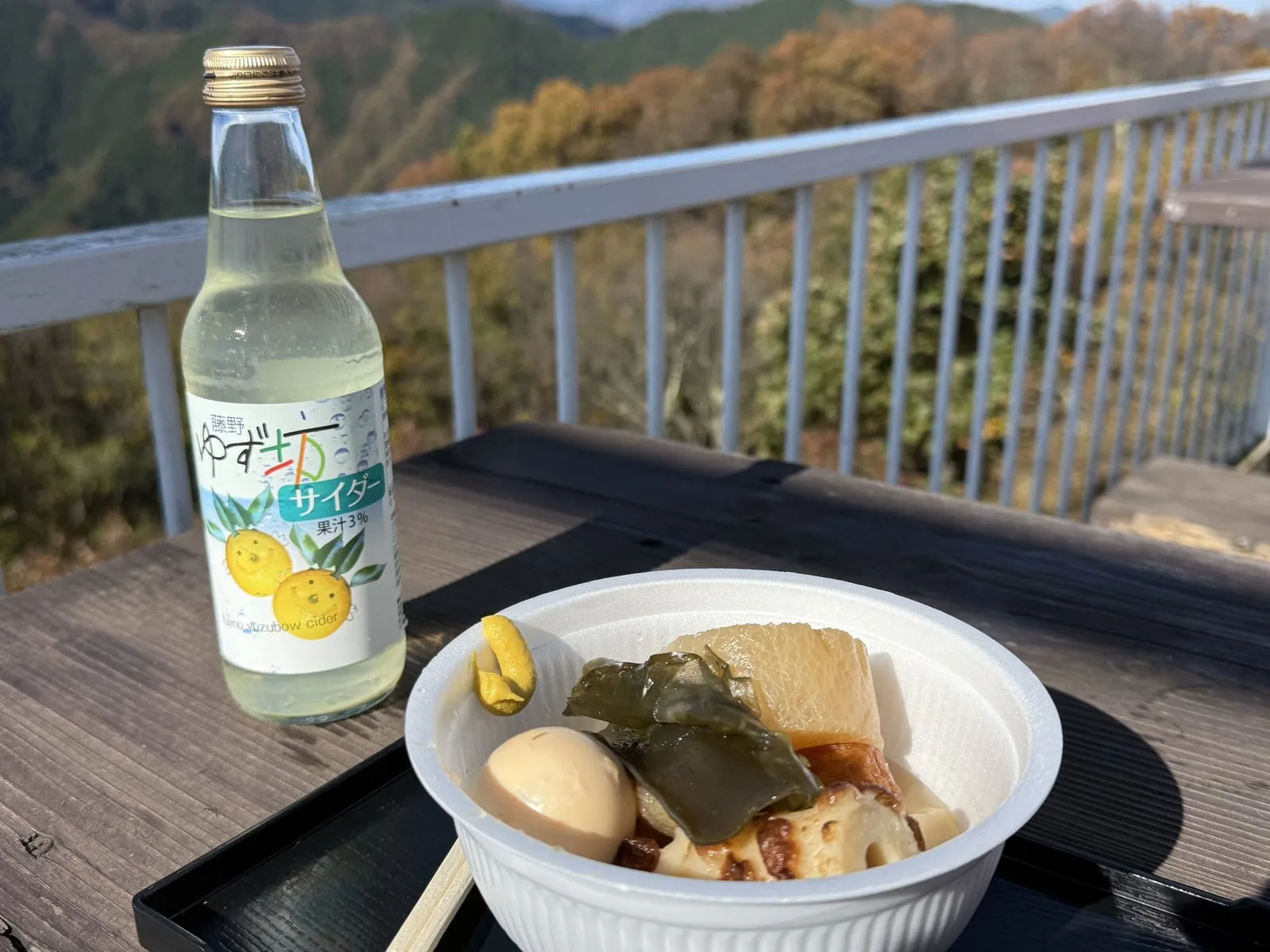 A bottle of yuzu cider and a bowl of oden on a terrace railing on Mt. Jinba