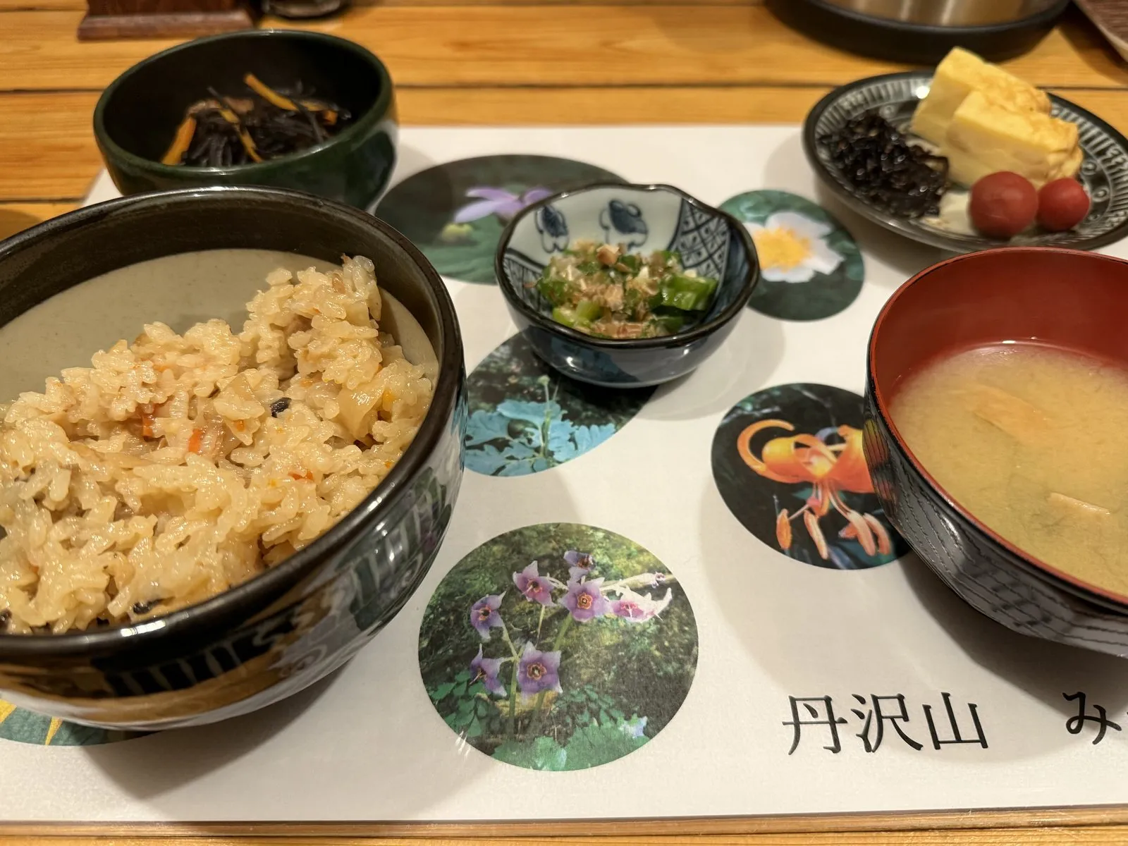 Breakfast at Miyama Sanso: seasoned mixed rice, miso soup, rolled omelette and small side dishes, on a placemat printed with mountain flowers